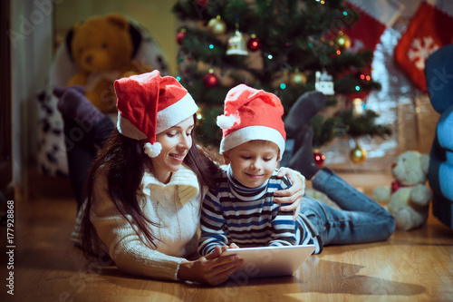 Young mother and a son using a tablet pc by a fireplace on warm Christmas evening