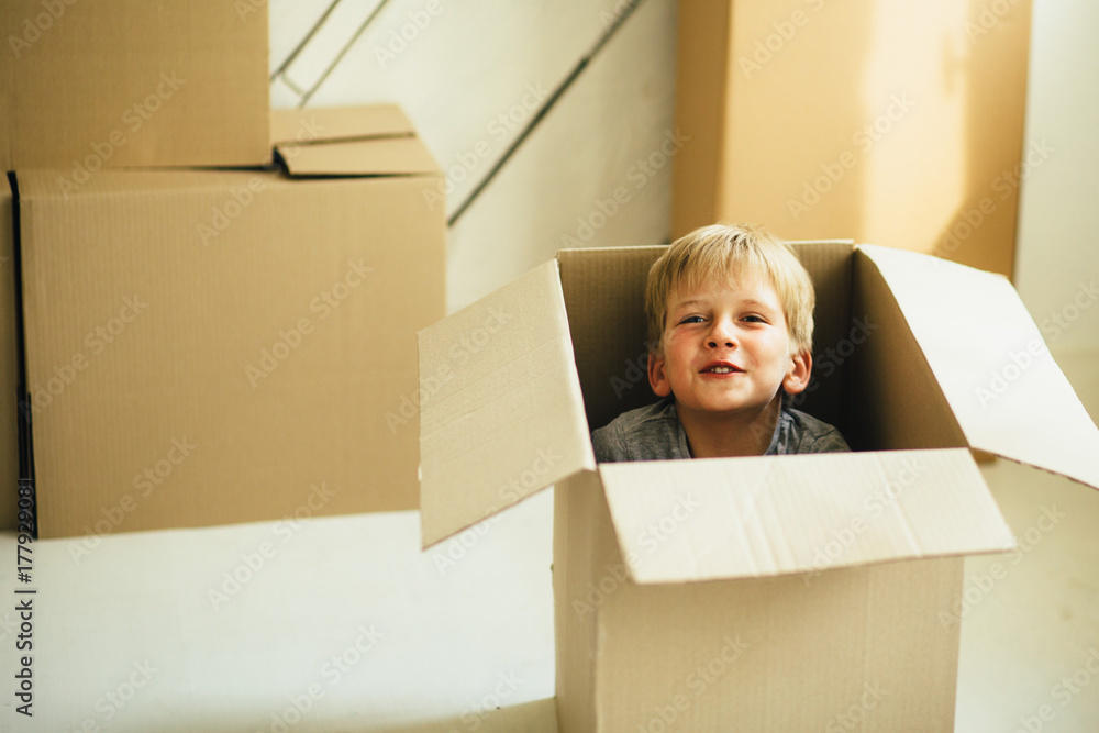 Rose cheeks preschooler boy sitting inside box in new house. Childhood, repairs and find new real estate concept. Rose cheeks preschooler boy sitting inside box in new house. Childhood, repairs and find new real estate concept.