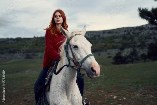 red-haired girl sitting on a white horse against a wildlife background
