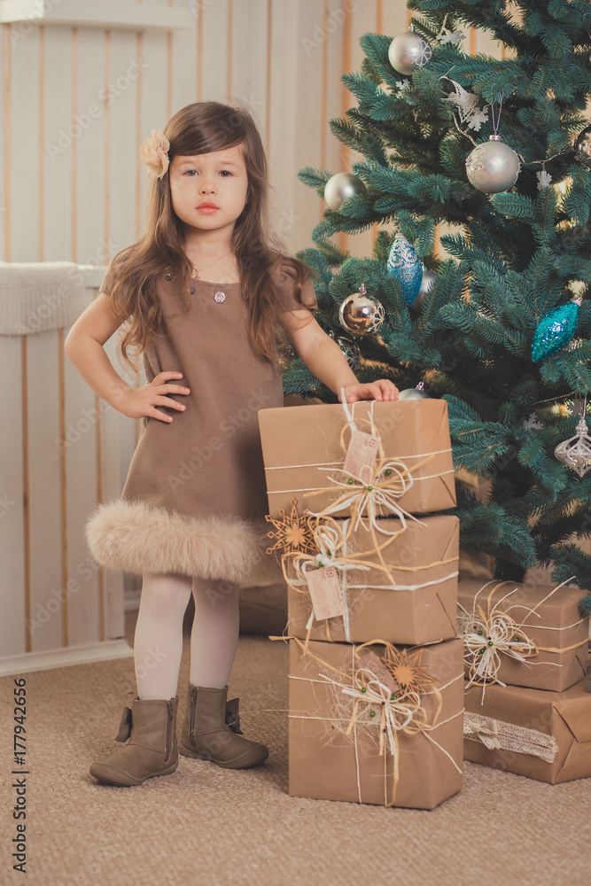 Young brunette dolly lady girl stylish dressed cozy warm winter gray jacket with fur posing sitting standing in studio close to Christmas New Year tree and presents. Young brunette dolly lady girl stylish dressed cozy warm winter gray jacket with fur posing sitting standing in studio close to Christmas New Year tree and presents.