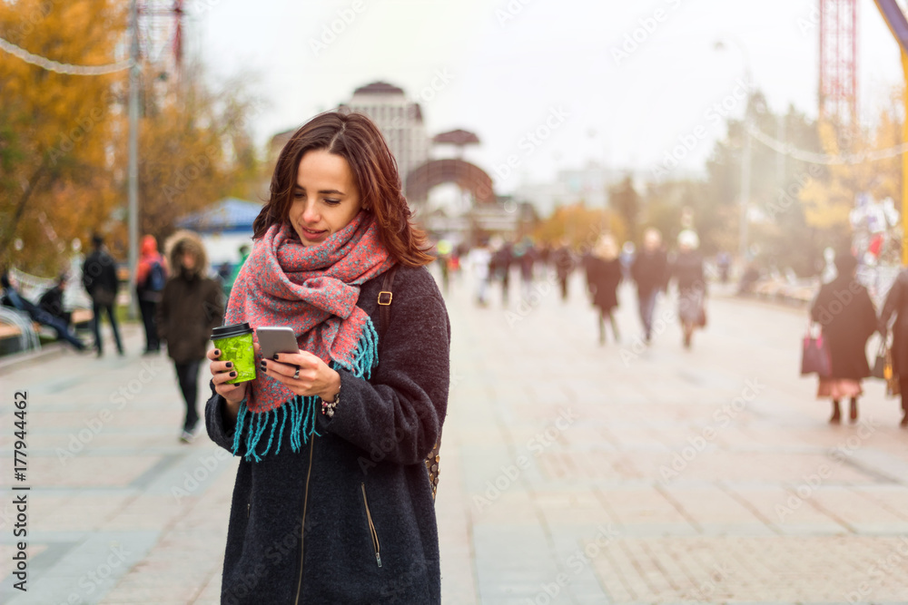 young beautiful brunette girl with coffee to go and smartphone on the background of blurred city street young beautiful brunette girl with coffee to go and smartphone on the background of blurred city street