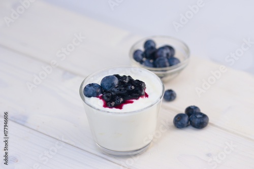 Glass cup of yogurt with blueberries on white table and white background