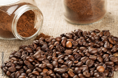 Roasted coffee beans and glass jar with ground coffee inside  closeup