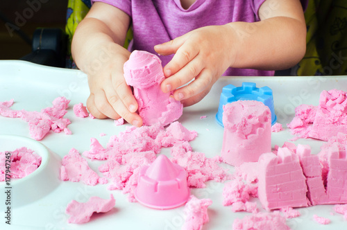Childs hands building castle from kinetic sand on the table