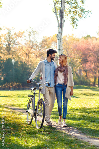 Young couple with bicycle walking in park on sunny autumn day.