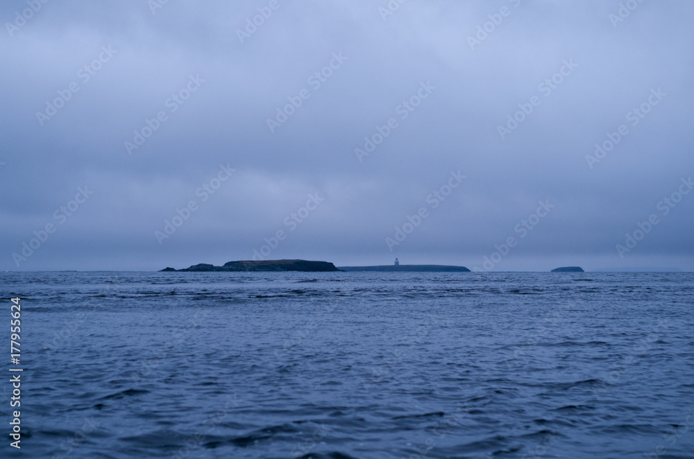 Arctic island in the Barents Sea, in the distance can be seen a lighthouse and rocks. Arctic island in the Barents Sea, in the distance can be seen a lighthouse and rocks.