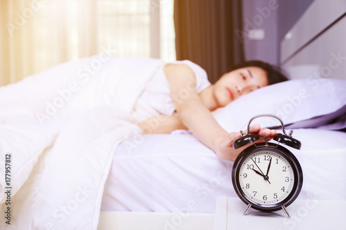 woman sleeping on bed and rise hand to turn off alarm clock in bedroom