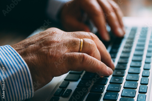 Detail of the hands of a senior businessman typing on a laptop keyboard photo