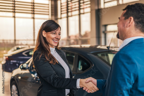 Cheerful car dealer handshake with customer in showroom. photo
