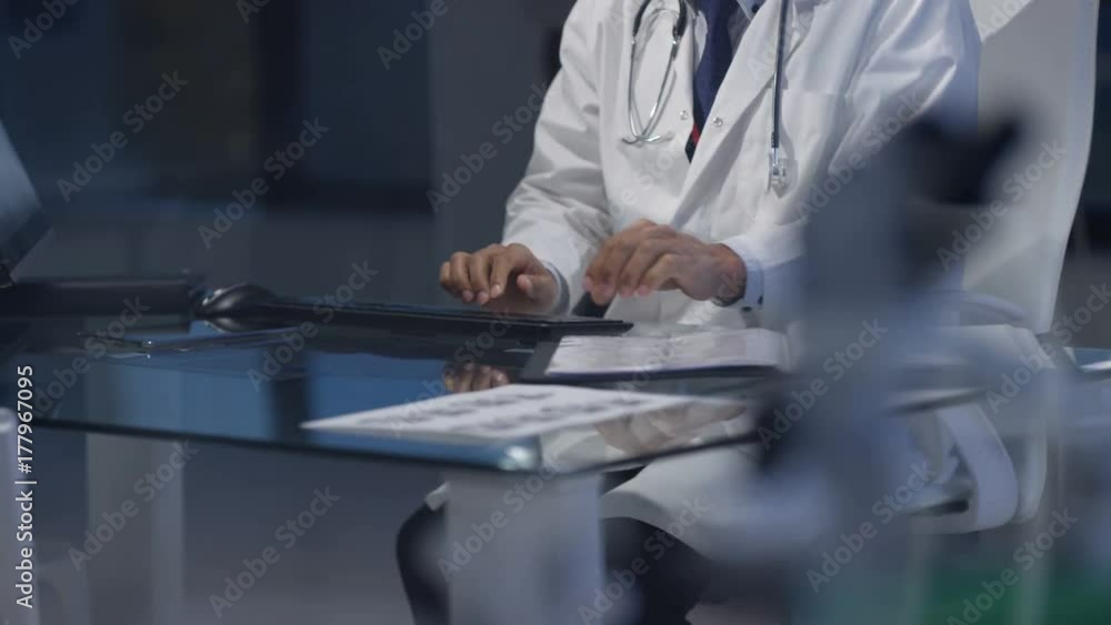 Doctor in modern hospital studying medical notes & working on computer Doctor in modern hospital studying medical notes & working on computer