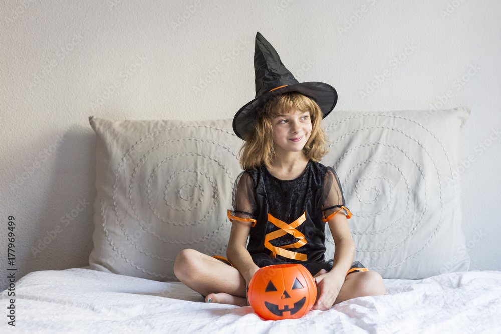 beautiful little girl smiling on bed and wearing a halloween costume. playing with pumpkins. Home, indoors, lifestyle beautiful little girl smiling on bed and wearing a halloween costume. playing with pumpkins. Home, indoors, lifestyle