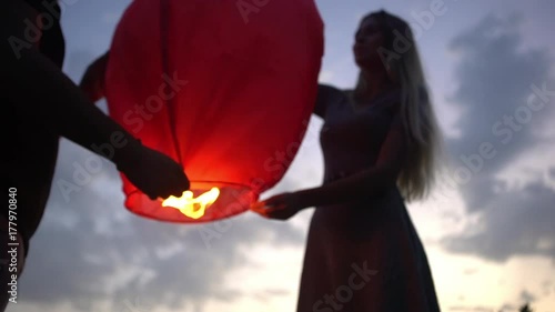 from beneath couple of young romantic people being on nature holding together burning chinese lantern want to launch it to evening sky in slow motion