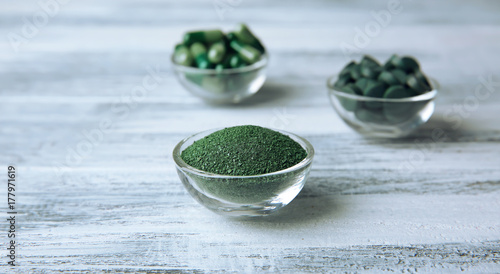 Bowls with spirulina powder  capsules and tablets on table