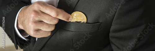 Businessman removing or placing a golden bitcoin in a pocket
