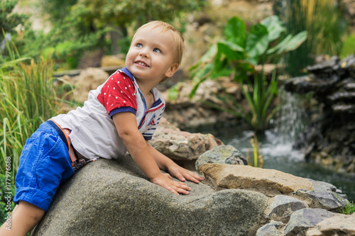 cute and beautiful 3 year old boy child smiles on a walk in the park by the pond on a sunny day photo