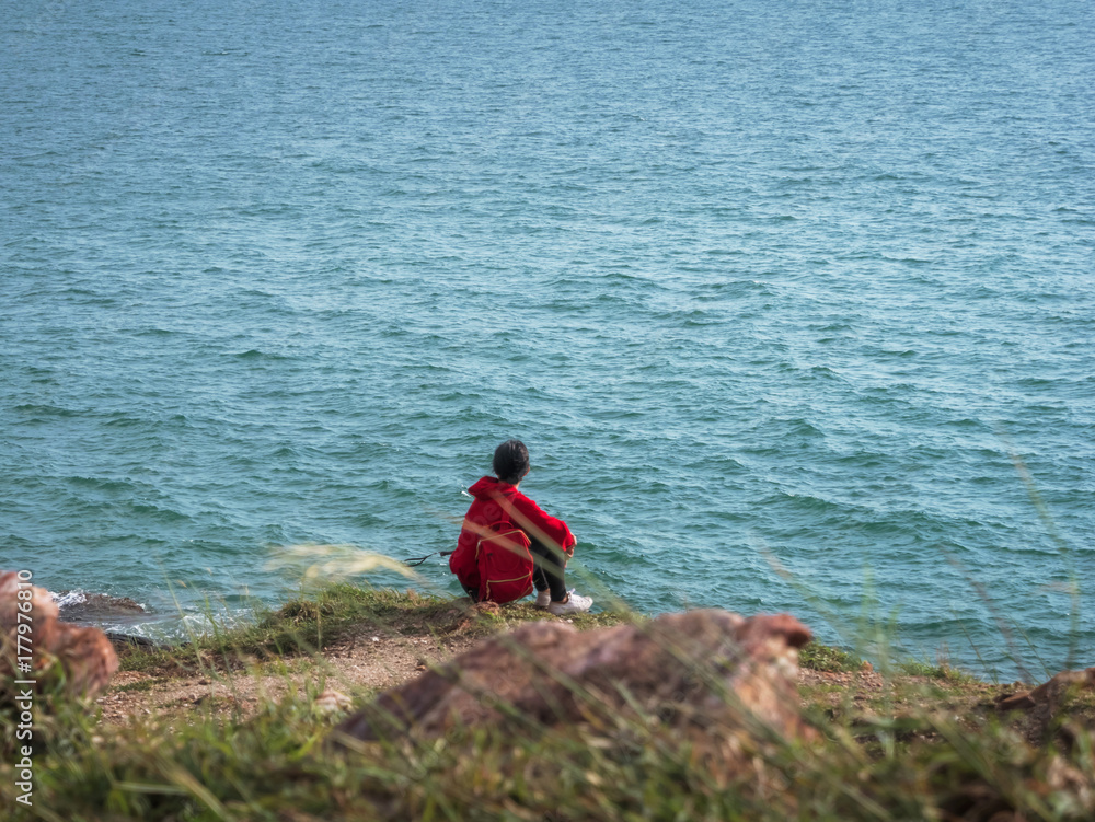 A woman wearing a red shirt sat watching the sea alone, she looked lonely.