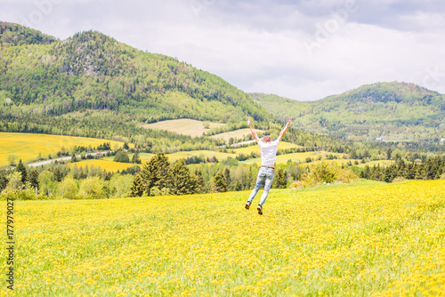 Young man, male running, jumping, hanging in air, mid-air and smiling on countryside yellow dandelion flower fields in summer grass in Ile D'Orleans, Quebec, Canada back