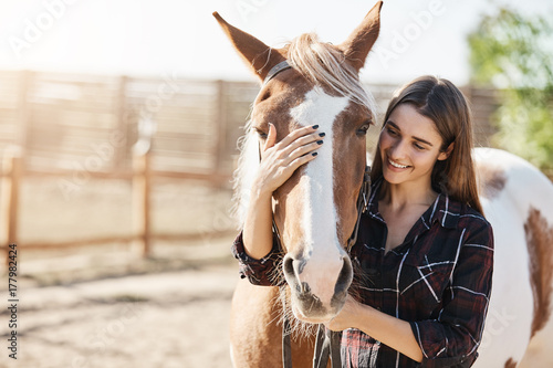 Canvas Print Young beautiful girl petting a horse taking care preparing to become a barn manager at an animal farm
