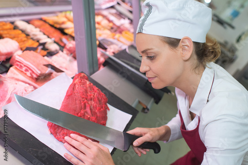 happy female butcher cutting meat at butchery counter