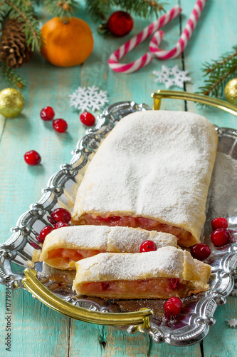 Homemade apple strudel with fresh apples, cranberries and sugar powder on the festive Christmas table. Apple strudel in a country style. photo