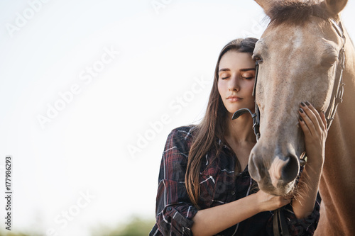 Portrait of a young girl interacting with a horse with closed eyes trying to calm the animal.