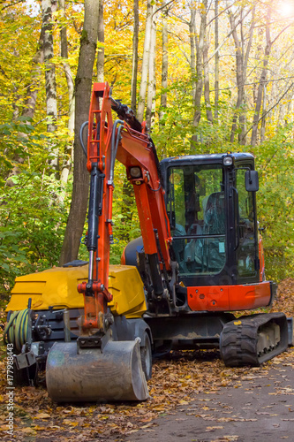 Red excavator at work making repair in park. Vertical