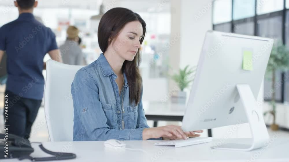 Portrait smiling young woman working on computer in creative office with colleagues talking in background. Shot on RED Epic. Portrait smiling young woman working on computer in creative office with colleagues talking in background. Shot on RED Epic.