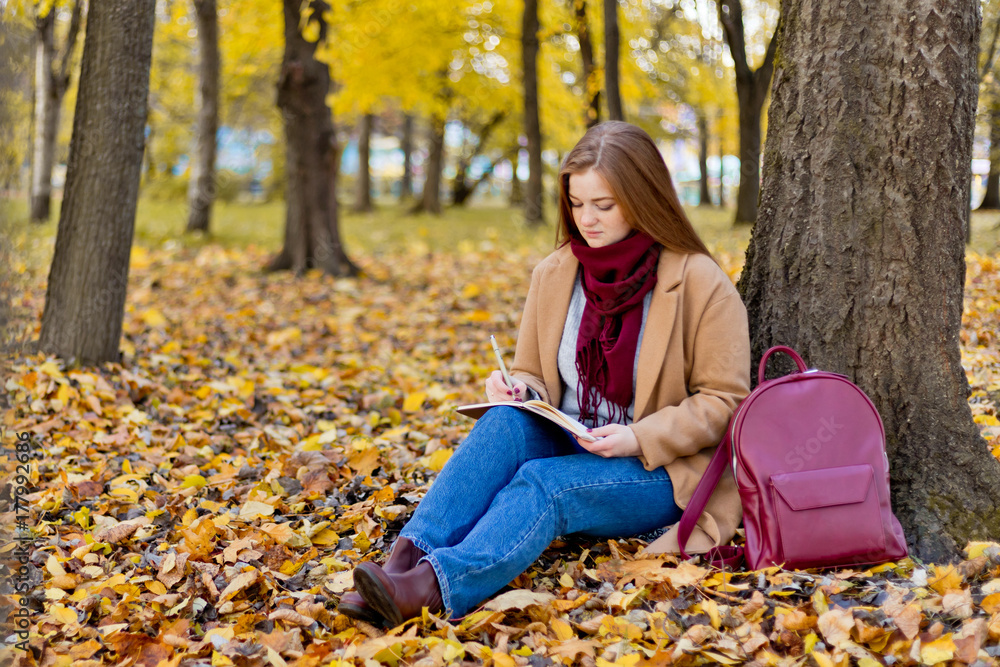 Girl sitting in the autumn park and writing about her life with notes Girl sitting in the autumn park and writing about her life with notes
