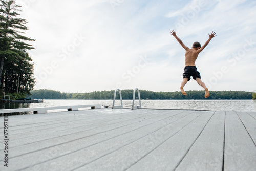Child jumps off a dock into a lake on a summer evening
