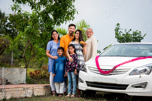 Indian family buying new car - Car buying or automobile boom concept in india, image representing asian family performing Pooja of newly purchased car or four wheeler at home wearing ethnic cloths

 photo