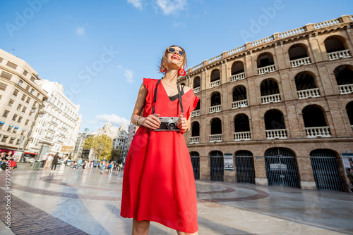 Portrait of young woman tourist in red dress standing with photo camera in front of the bullring amphitheatre in Valencia city, Spain © rh2010
