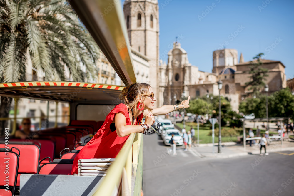 Young happy woman tourist in red dress having excursion in the open touristic bus in Valencia city, Spain