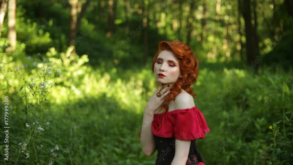Beautiful red-haired girl in red dress posing on green background. Portrait of a woman with red hair in a summer forest Beautiful red-haired girl in red dress posing on green background. Portrait of a woman with red hair in a summer forest