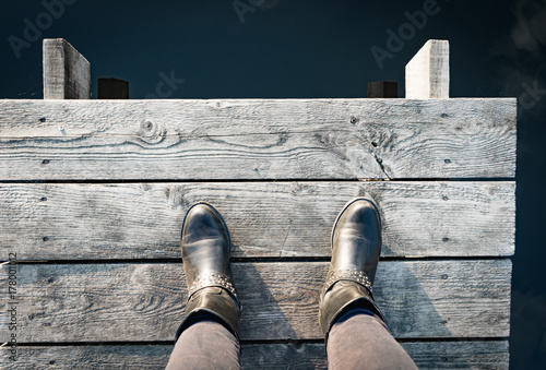 woman in boots on the pier takes a step into the water, from above,