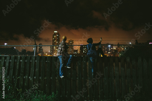 two people climbing over a fence at night
