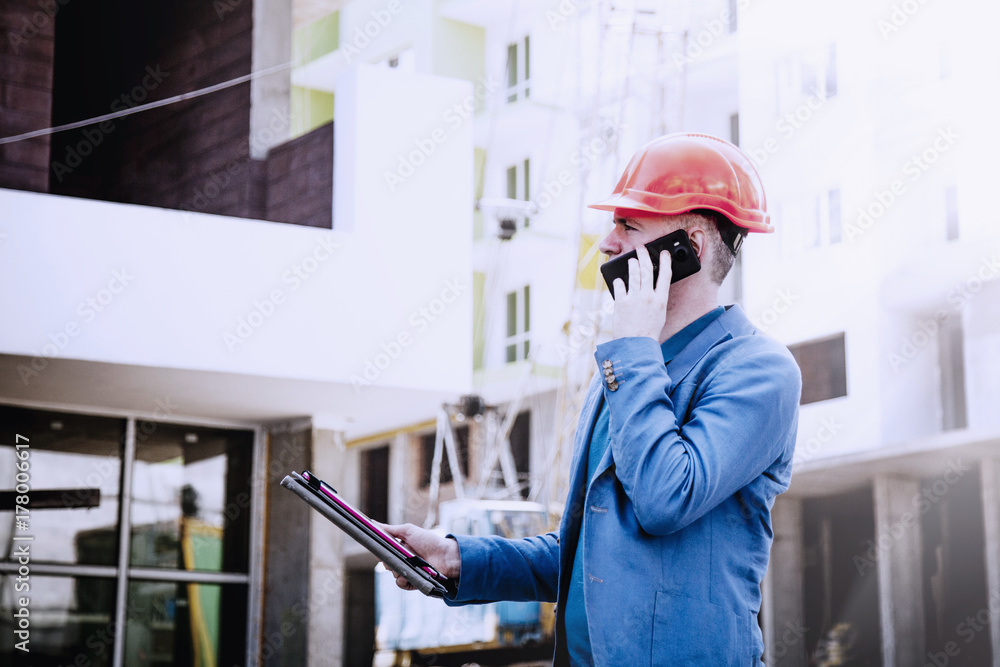 Young engineer man in suit and helmet talking mobile phone on construction site (engineer, construction worker concept) Young engineer man in suit and helmet talking mobile phone on construction site (engineer, construction worker concept)