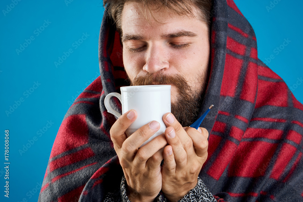 a man in a plaid warmth drinks hot tea on a blue background, is ill with the flu a man in a plaid warmth drinks hot tea on a blue background, is ill with the flu