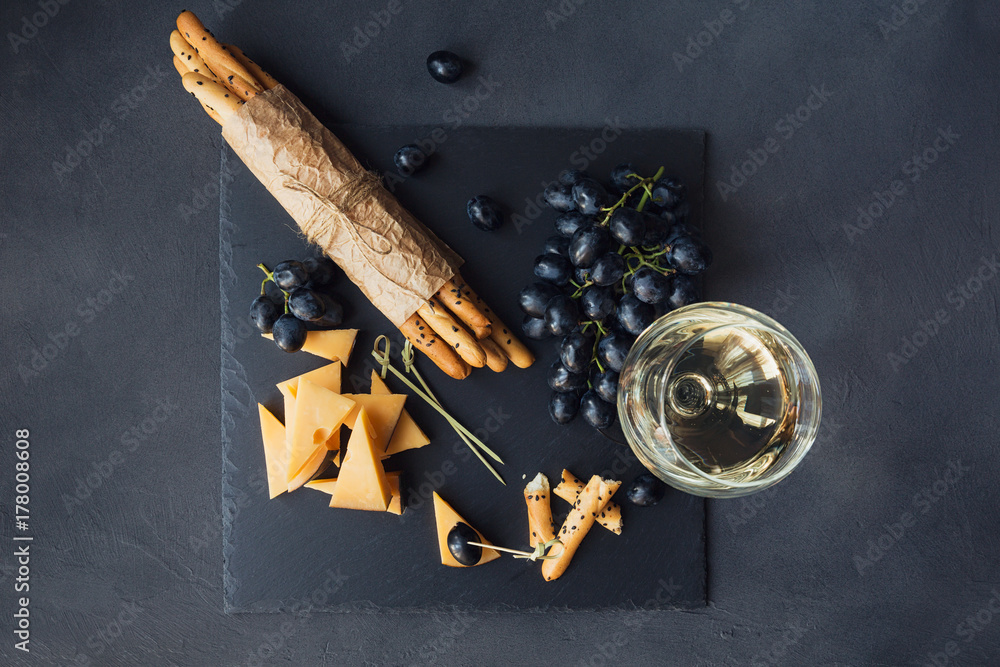Cheese plate served with crackers, grapes and glass of white wine on dark background. - obrazy, fototapety, plakaty 