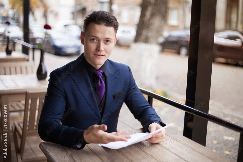 A wealthy young businessman in a suit offers a contract at a cafe. Signing of the marriage contract before the wedding.