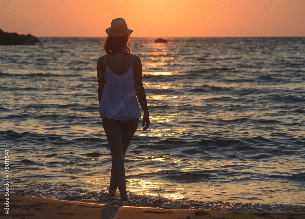 Φωτογραφία Young woman walking on the beach by the sea at summer sunset