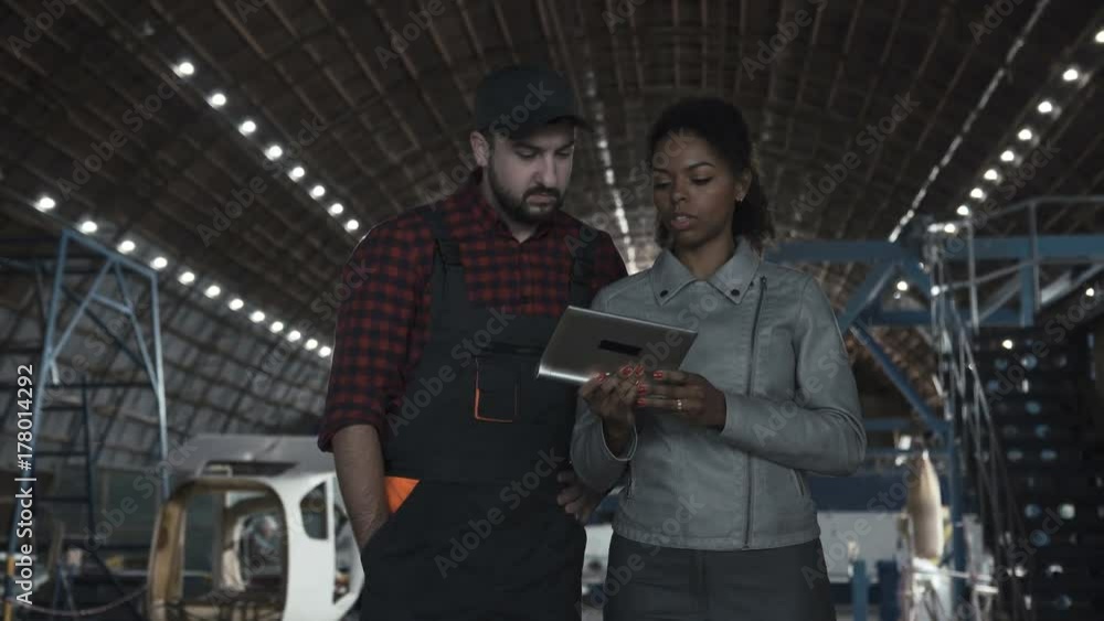 Man standing and discussing over digital tablet in aircraft hangar with woman Man standing and discussing over digital tablet in aircraft hangar with woman