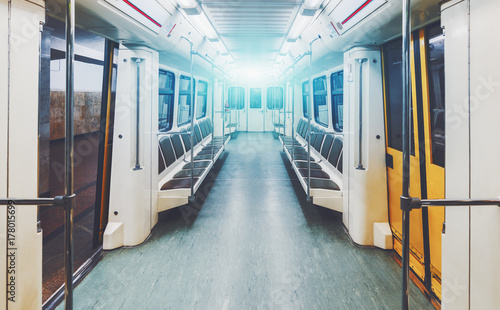View of bright empty interior of modern subway train car while it is waiting on station with yellow doors opened; contemporary underground railway carriage indoors with no one inside, empty seats