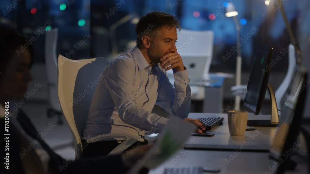Tired businessman working late, working on computer at his desk Tired businessman working late, working on computer at his desk