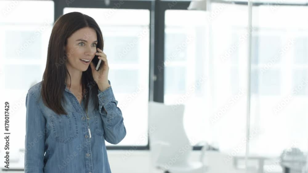 Businesswoman in young startup company talking on phone before a meeting with colleagues. Shot on RED Epic. Businesswoman in young startup company talking on phone before a meeting with colleagues. Shot on RED Epic.