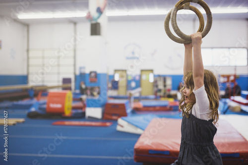 Cute preschool girl hanging on rings at gymnastics photo