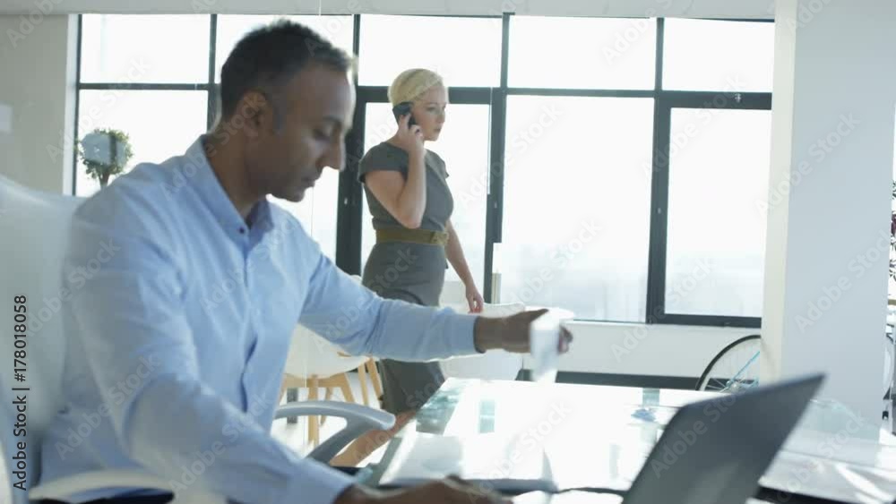 Corporate businessman working on laptop in office and woman talking on phone Corporate businessman working on laptop in office and woman talking on phone