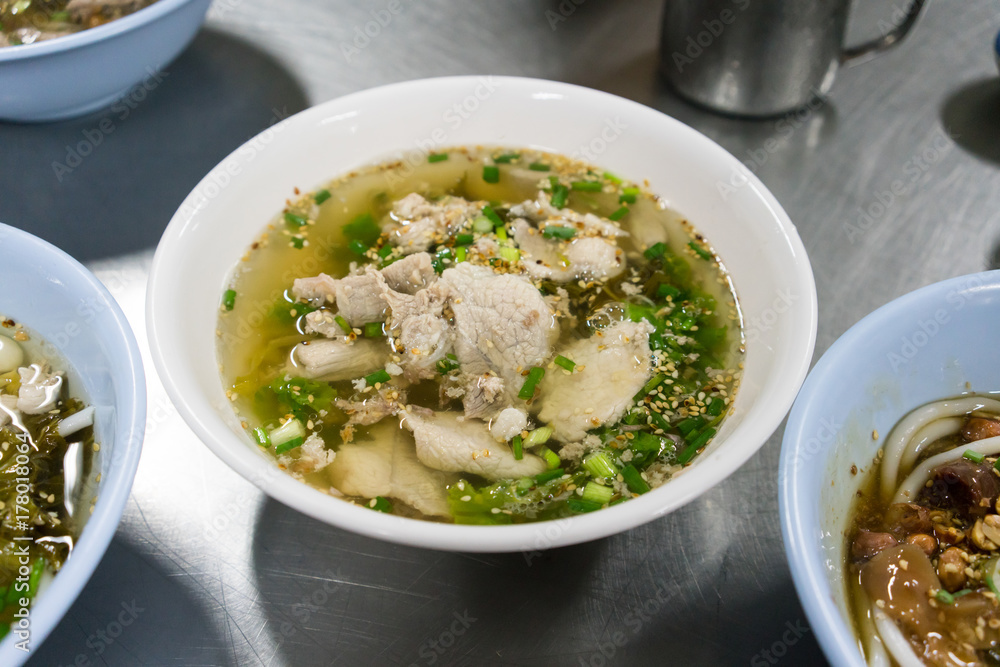 A bowl of Hainan rice noodle with pork in Thai style on stainless steel table.