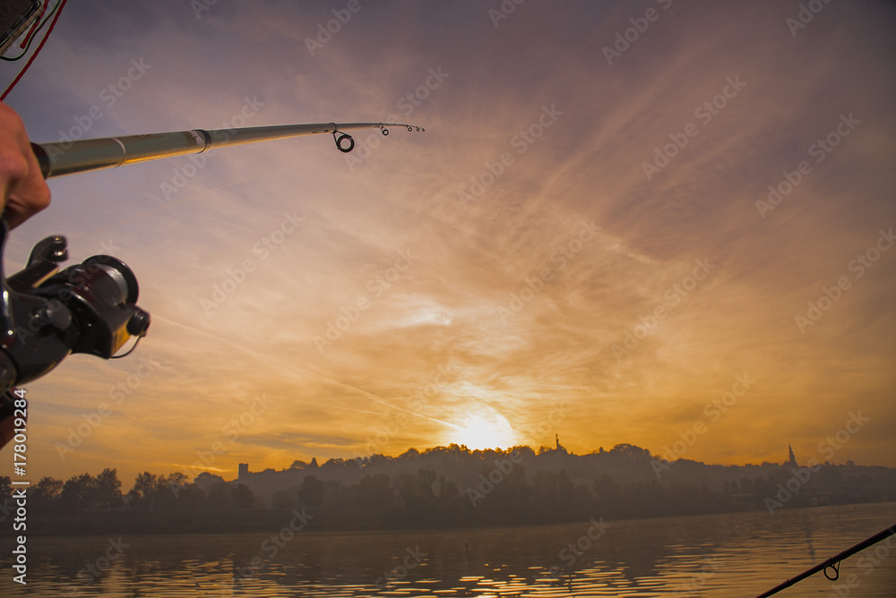 Φωτογραφία Fishing rod wheel closeup, man fishing with a beautiful sunrise behind him