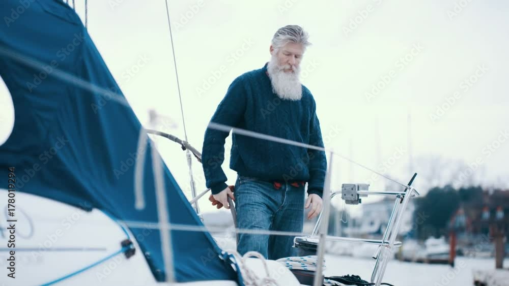 Mature bearded man with boat docked in marina, preparing for a sailing trip Mature bearded man with boat docked in marina, preparing for a sailing trip