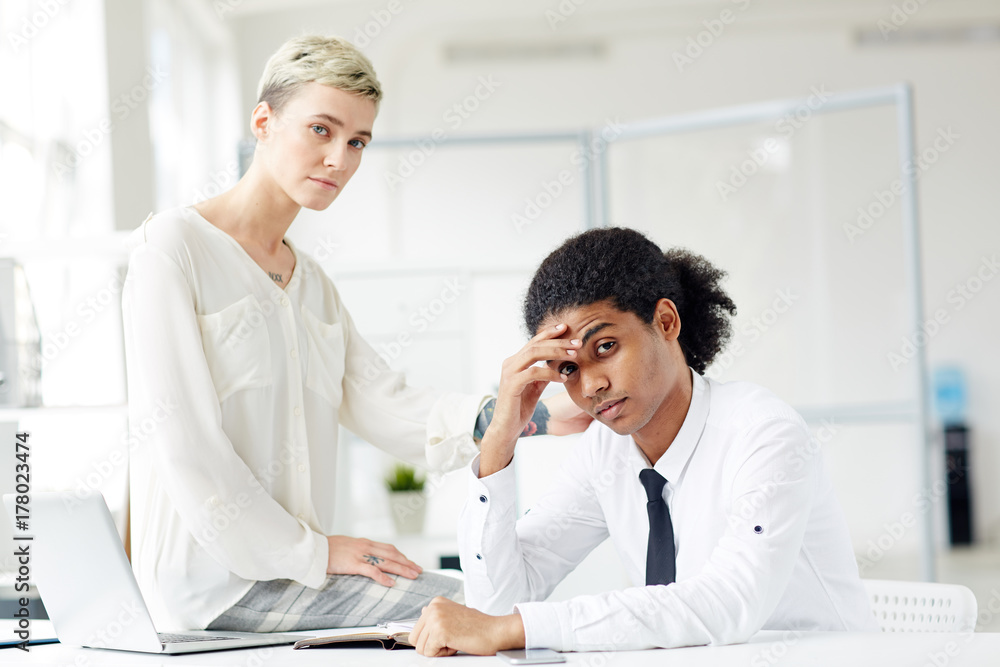 Upset intercultural colleagues looking at camera during work in office Upset intercultural colleagues looking at camera during work in office